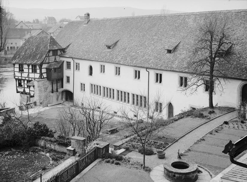 View from high-up of a garden and monastery buildings. There are plain tiles on the roofs. The walls are newly plastered. The garden has been newly arranged. Photo in black and white.